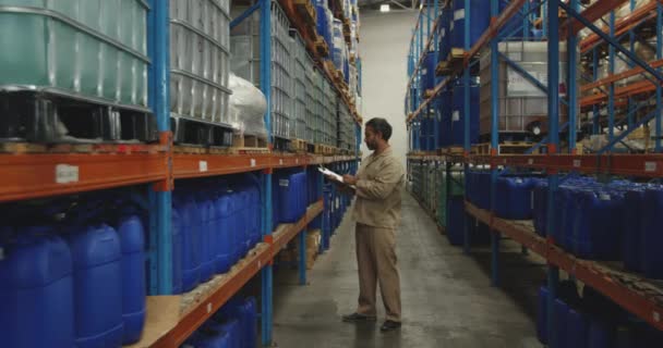 Vue latérale d'un ouvrier d'entrepôt mixte d'âge moyen effectuant une inspection et écrivant sur un presse-papiers dans un entrepôt de stockage 