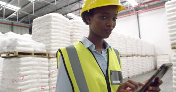 Portrait gros plan d'une jeune gérante d'entrepôt mixte portant un casque jaune à l'aide d'un ordinateur tablette dans un entrepôt et souriant à la caméra 