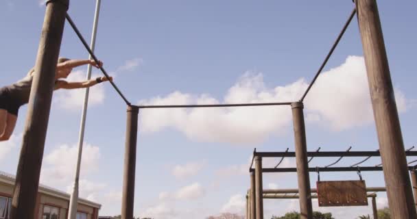 ブートキャンプトレーニングセッション中に屋外ジムでクライミングフレーム上のバーの間でスイングし ジャンプ若い白人女性の側面図 — ストック動画