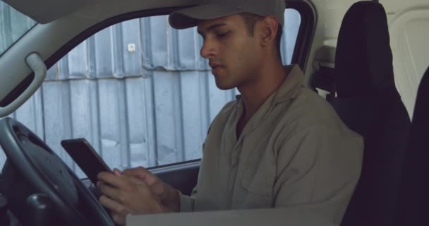 一个年轻的混血男性仓库工人坐在一辆面包车的驾驶座上 在仓库外使用平板电脑的侧视图特写 — 图库视频影像