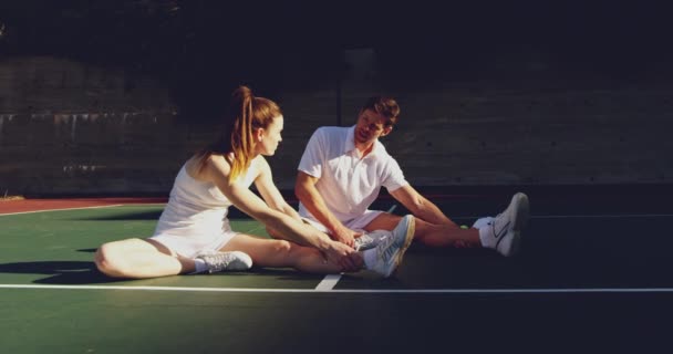 若い白人女性と若い白人男性がコートでテニスをしたり 試合前にストレッチをしたり 話したりする正面図 — ストック動画