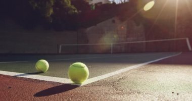Güneşli bir tenis kortundan yuvarlanan iki tenis topunun yakın çekim