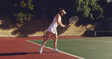 Genç beyaz bir kadın ve kortta tenis oynayan genç bir Beyaz adamın yan görünümü, top zıplatan ve hizmet eden kadın