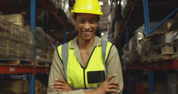 Portrait gros plan d'une jeune ouvrière d'entrepôt de race mixte portant un casque jaune debout avec les bras croisés, regardant la caméra sourire dans un entrepôt de stockage 
