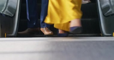 Modern bir ofis binasının güneşli lobisinde yürüyen merdivenden inen iş adamlarının bacakları düşük açılı görüntüsü.