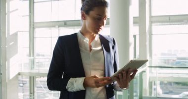 Modern bir ofis binasının güneşli lobisinde duran bir tablet bilgisayar kullanarak genç bir Kafkas iş kadını yan görünümü yakın