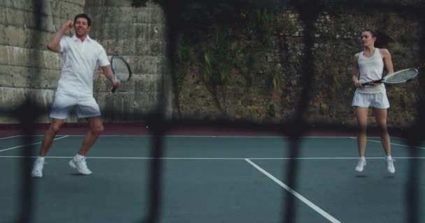 若い白人女性とコートでテニスをしている若い白人男性の正面図 勝つとネットを通して見て — ストック動画