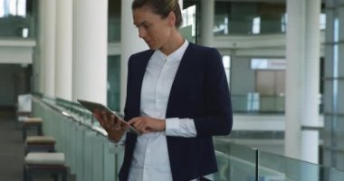 Modern bir ofis binasının lobisinde duran bir tablet bilgisayar kullanarak gülümseyen genç Kafkas iş kadını yan görünümü yakın