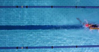 Yüzme havuzunda eğitim gören genç bir kadın yüzücünün tepeden görünümü, sırtüstü