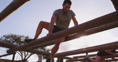 Beyaz bir kadın ve beyaz bir genç adamın, bir acemi birliği eğitim seansı sırasında, bir spor salonunun tepesinde direkler arasından tırmanışlarının düşük açılı görüntüsü.