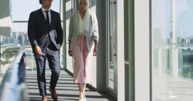 Onlar güneşli modern bir ofis binasında bir koridorda yürürken genç bir Cacuasian işadamı ile konuşurken bir türban giyen genç bir karışık ırk iş kadını Ön görünümü