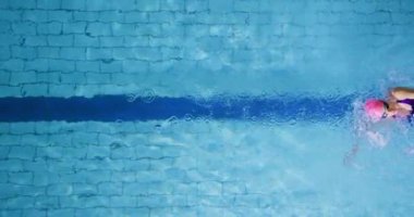 Yüzme havuzunda eğitim gören genç bir kadın yüzücünün tepeden görünümü, sırtüstü