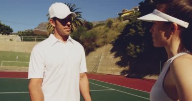 Yan görüş yakın genç bir Kafkas kadın ve genç bir Kafkas adam bir kortta tenis oynarken, konuşurken