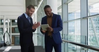 Genç bir Afro-Amerikalı işadamı ve Kafkasyalı genç bir işadamının modern bir ofiste konuşurken, gülümserken ve bir tablet bilgisayarına bakarken