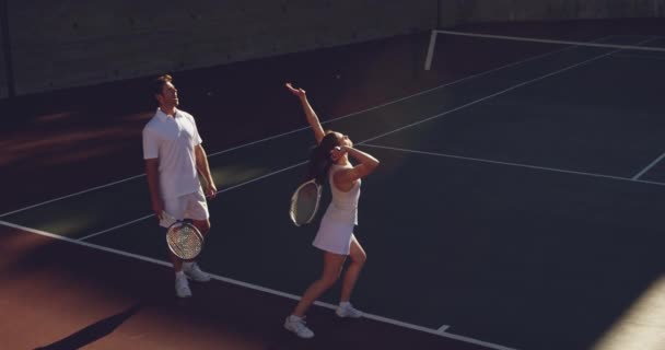 若い白人女性とコートでテニスをしている若い白人男性の高角リアビュー 女性が奉仕 — ストック動画