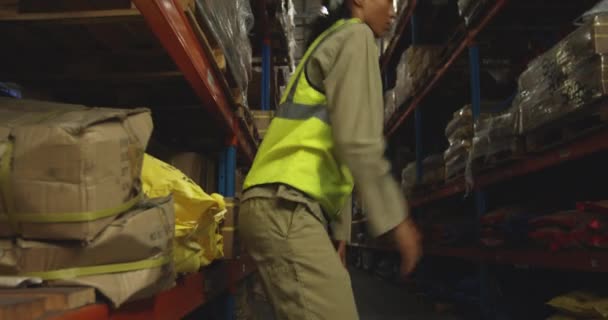 一位年轻的混血女仓库工人摘下硬帽 坐下来在仓库的货架之间歇息 侧观近景 — 图库视频影像