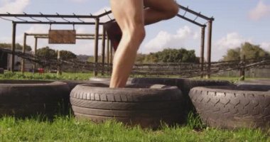 Bir acemi birliği eğitim seansı sırasında açık hava spor salonunda lastiklere basan iki beyaz kadının yan görüntüsü.