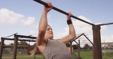 Bir acemi birliği eğitim seansı sırasında spor salonunda barfiks çeken beyaz bir kadının yan görüntüsü.