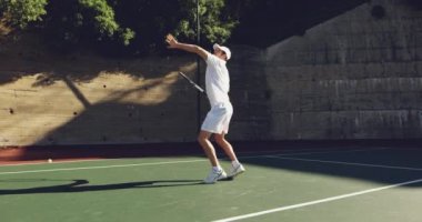 Güneşli bir günde tenis oynayan, topu geri dönen beyaz bir adamın yan görünümü