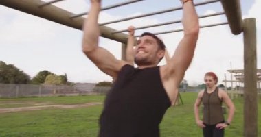 Acemi kampı eğitiminde iki beyaz kadın ve bir beyaz adamın açık hava spor salonundaki maymun parmaklıklarını kullanışının ön görüntüsü.