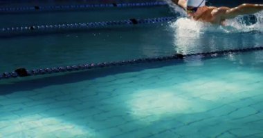 Yüzme havuzunda eğitim gören beyaz erkek yüzücünün yan görünümü, kelebek