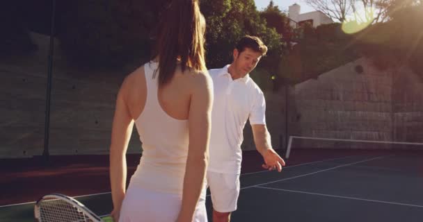 若い白人女性とコートでテニスをしている若い白人男性の背面図 — ストック動画