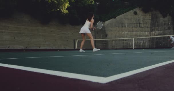 若い白人女性とコートでテニスをしている若い白人男性の背面図 ボールを返す女性 — ストック動画