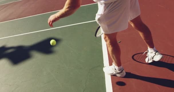 コートでテニスをしている若い白人男性のサイドビュークローズアップ サーブの準備をするボールをバウンス — ストック動画
