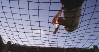 Bir acemi birliği eğitim seansı sırasında açık hava spor salonunda ağların üzerinden tırmanan beyaz bir adamın alçak açılı görüntüsü.