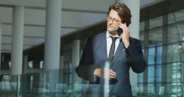 Modern bir ofis binasında güneşli bir yerde duran bir akıllı telefon üzerinde konuşurken gülümseyen genç Kafkas işadamı yan görünümü