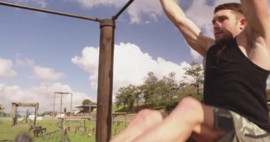 Bir acemi birliği eğitim seansı sırasında, açık hava spor salonunun tepesinde asılı duran genç bir beyaz adamın ön görüntüsü.