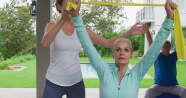 Genç bir Kafkas kadın fitness eğitmeni ile, bir bahçede lastik bantlar ile egzersiz üst düzey bir Kafkas kadın ve adam Ön görünümü