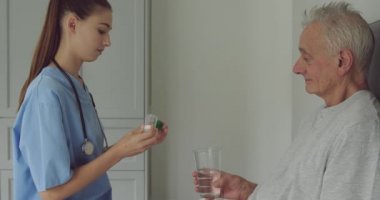 Yatakta yatan kıdemli bir Beyaz adam ve hastanede ona ilaç veren genç bir Kafkas kadın hemşirenin yan görünümü
