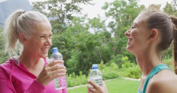 庭での運動の休憩中に水を飲む若い白人女性フィットネスインストラクターの先輩白人女性の正面図クローズアップ — ストック動画