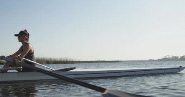 Eğitim sırasında nehirüzerinde yarış kabuğunda kürek çekerek kürek çekerek iki genç yetişkin Kafkas kadının yan görünümü