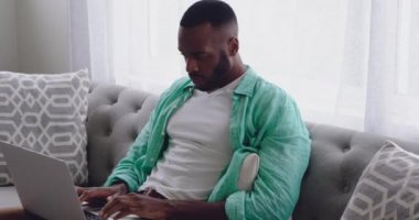 Evde bir dizüstü bilgisayar kullanarak kanepede oturan genç bir yetişkin karışık ırk adam ön görünüm yakın