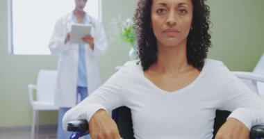 Hastanede ki koğuşta tekerlekli sandalyede oturan Afro-Amerikan engelli kadın hastayakın çekim. Dijital tablet kullanan Beyaz kadın doktor, video