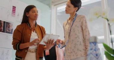 Modern bir ofiste çalışan, tablet kullanarak ve kumaş seçiminde çalışan mutlu genç Kafkas ve karışık ırk kadın iş kreatiflerinin ön görünümü