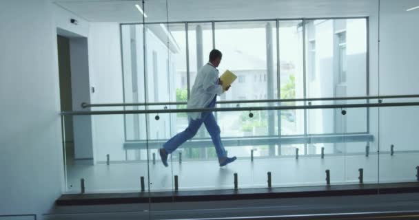病院の廊下を走る多様な男性と女性の医師の側面図 医療ファイル ビデオを保持している — ストック動画