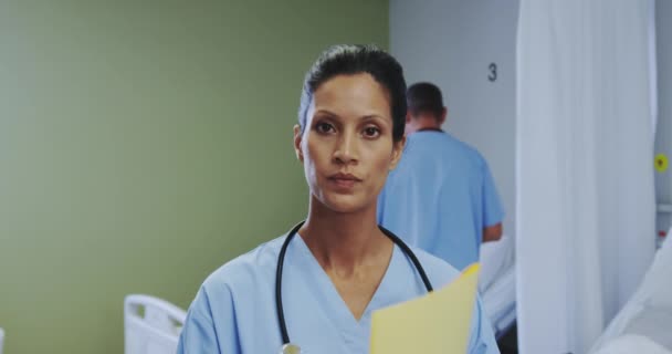 在医院的病房里 非洲裔美国女医生在看摄像机的正面视角 男医生与女病人在床上交谈 — 图库视频影像