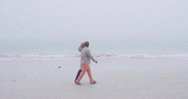 El ele tutuşan ve deniz kenarında bir plajda yürüyen olgun bir karışık ırk çift yan görünümü