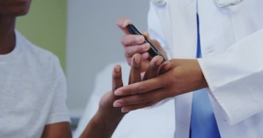 Afro-Amerikan kadın doktorun yakın çekim hastane koğuşunda erkek hastanın şeker seviyesini kontrol ediyor. O glucometer kullanıyor, video