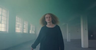 Boş bir depoda bir kalça genç Kafkas kadın ön görünümü, bir el bombası yeşil duman içinde yürüyor