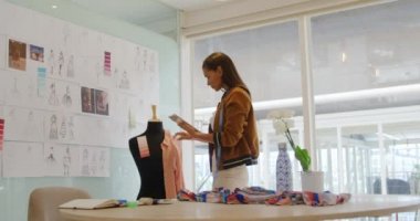 Mutlu bir genç karışık ırk kadın iş yaratıcı modern bir ofiste çalışan yan görünümü, bir tablet kullanarak ve moda tasarımları için renkleri kontrol