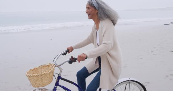 海辺のビーチで自転車に乗る幸せな成熟した混合レースの女性の側面図 — ストック動画