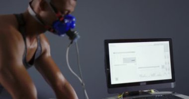 Yan görünüm yakın eğitim sırasında bir metabolik gaz analizörü kullanarak genç bir karışık ırk erkek bisikletçi, yanında bir bilgisayar monitörü ile bir yüz maskesi giyiyor