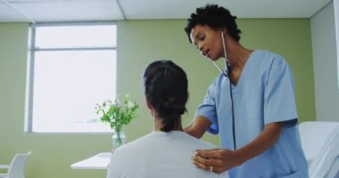 Hastanede koğuşta kadın hasta muayene Afrikalı Amerikalı kadın doktor yan görünümü. O stetoskop kullanıyor, video
