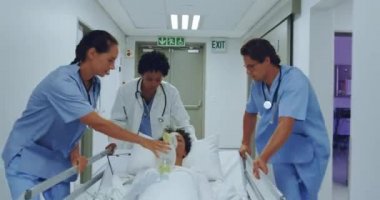 Hastane koridorunda acil sedye yatağını iten çeşitli sağlık ekibinin ön görünümü. Oksijen maskesi tutan kadın doktor, video