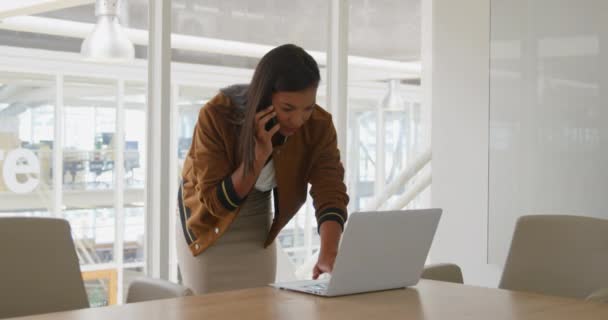 在现代办公室工作 使用笔记本电脑和在智能手机上交谈的快乐年轻混血女性商业创意的前沿视图 — 图库视频影像