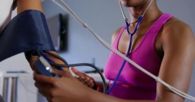 Genç bir Afro-Amerikan kadın kişisel eğitmen kan basıncı kontrol ederken bir yüz maskesi giyen, eğitim sırasında bir metabolik gaz analizörü kullanarak genç bir karışık ırk kadın bisikletçi yakın